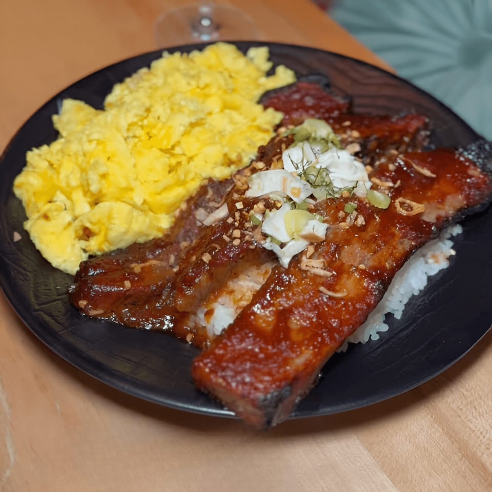 A black plate of DaVinci & Yu's Asian-fusion ribs with rice, scrambled eggs, and garnishes.