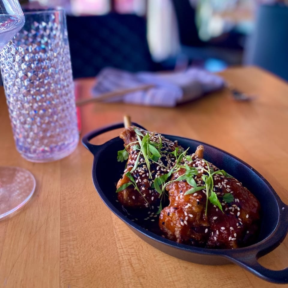 Asian-fusion chicken lollipops with sesame seeds and microgreens in a black dish on a wooden table.