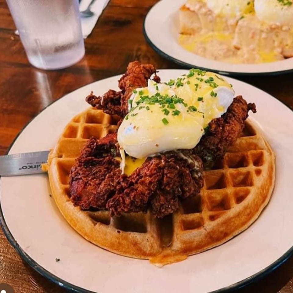 Crispy fried chicken and poached eggs with hollandaise sauce on a waffle, with another dish in the background.