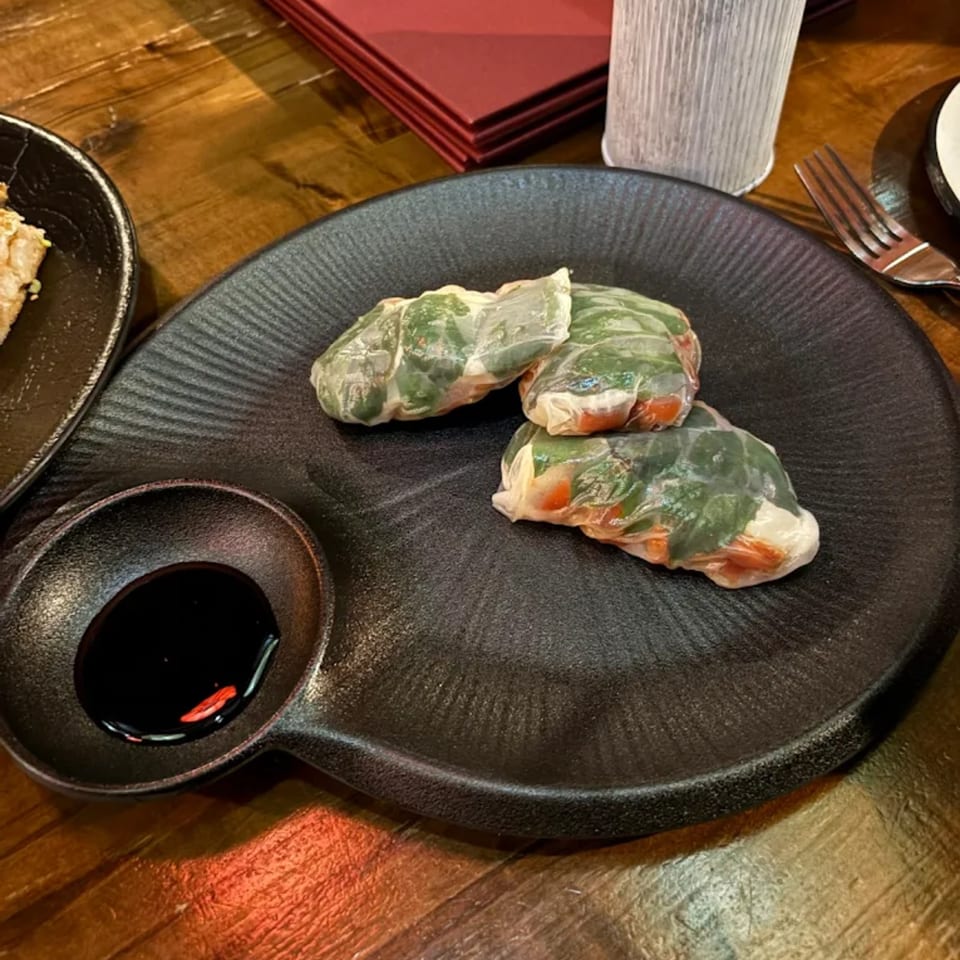 Three fresh spring rolls with green herbs and red filling, served with a dark dipping sauce.
