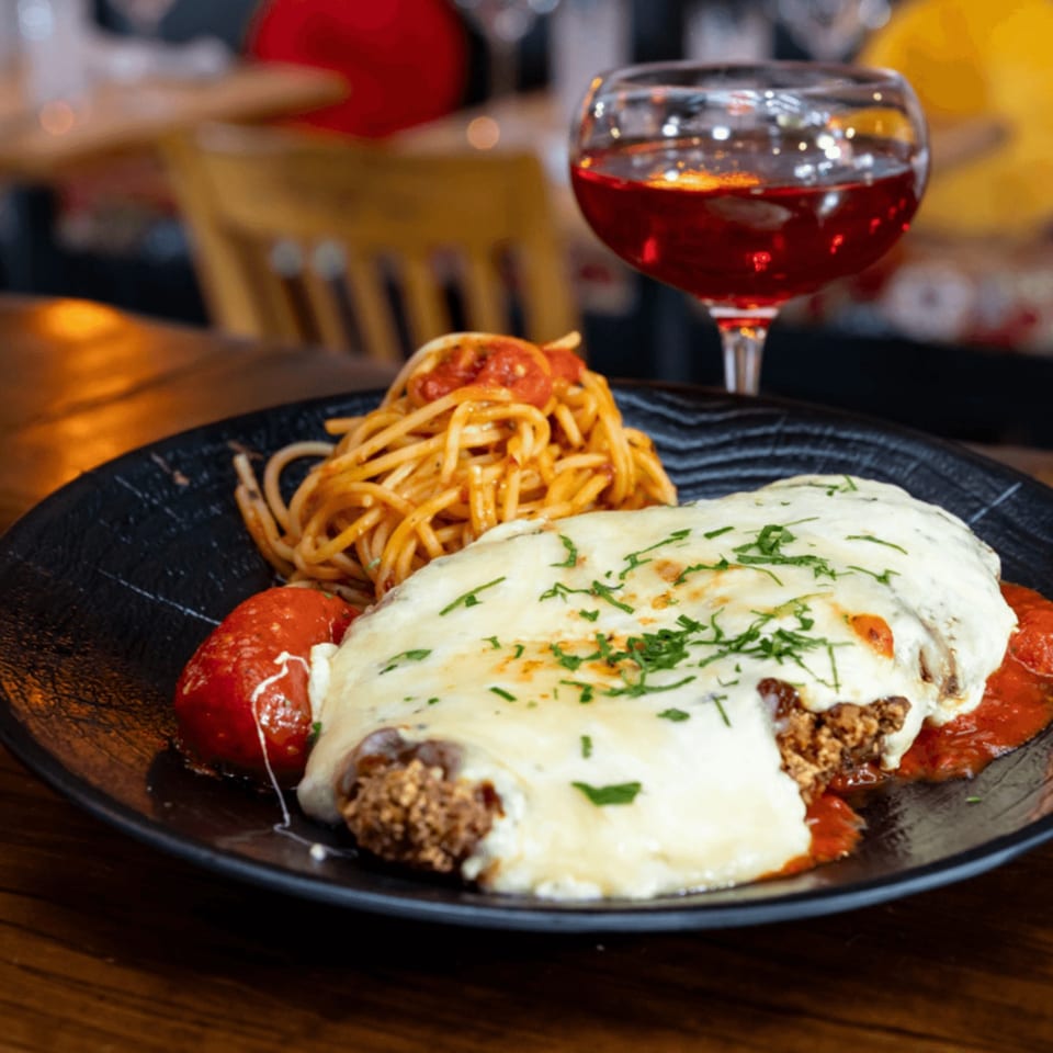 Chicken parmesan with spaghetti and a glass of red wine on a dark plate.